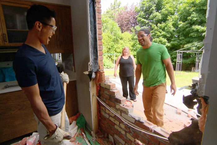 a large hole in a side of a house with one person inside and two people standing outside