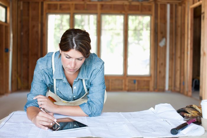 female construction professional using digital tablet in unfinished room of house